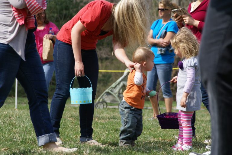 Mom holds young boy's hand while he stands in front of girl with Easter basket