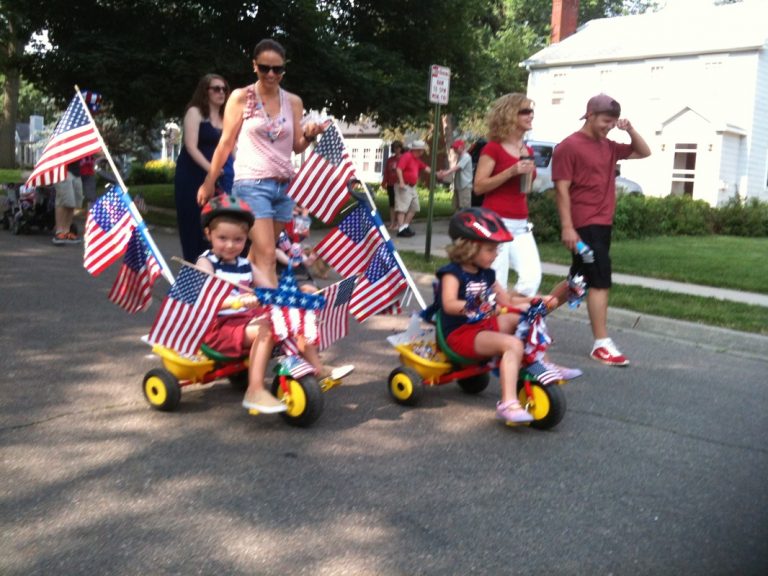 Two kids on tricycles decorated with numerous flags for ECCO 4th of July Parade 2015