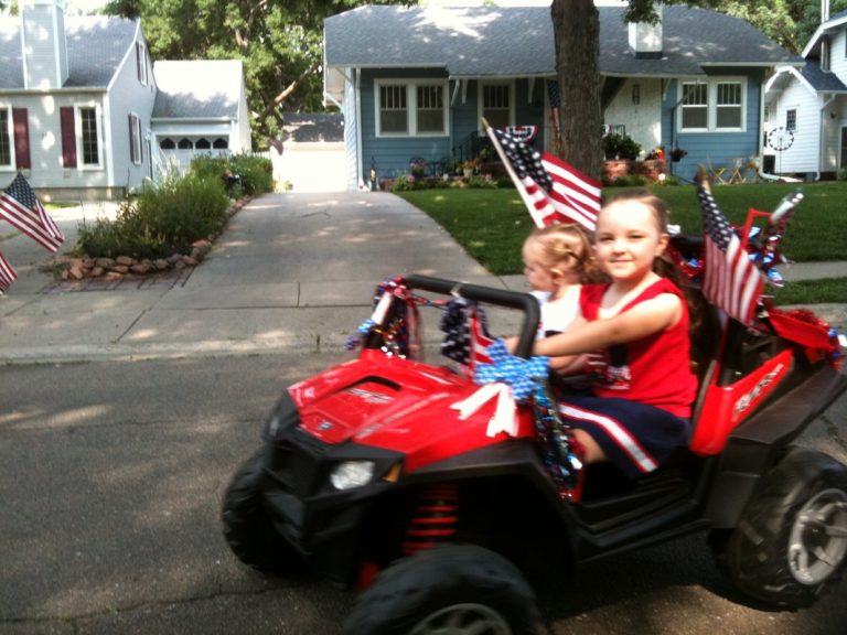 Two young girls drive a toy car decorated for the ECCO 4th of July Parade 2015