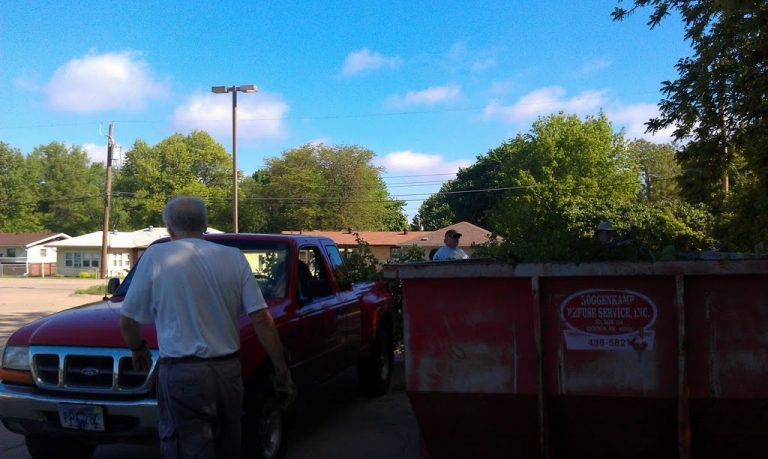 Dumpster filled with brush next to a pickup truck filled with brush
