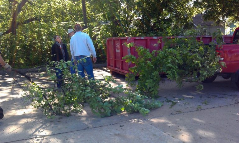 Dumpster filled with brush next to a pickup truck filled with brush